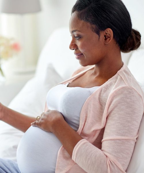 pregnancy, technology, people and expectation concept - happy pregnant african american woman with tablet pc computer in bed at home